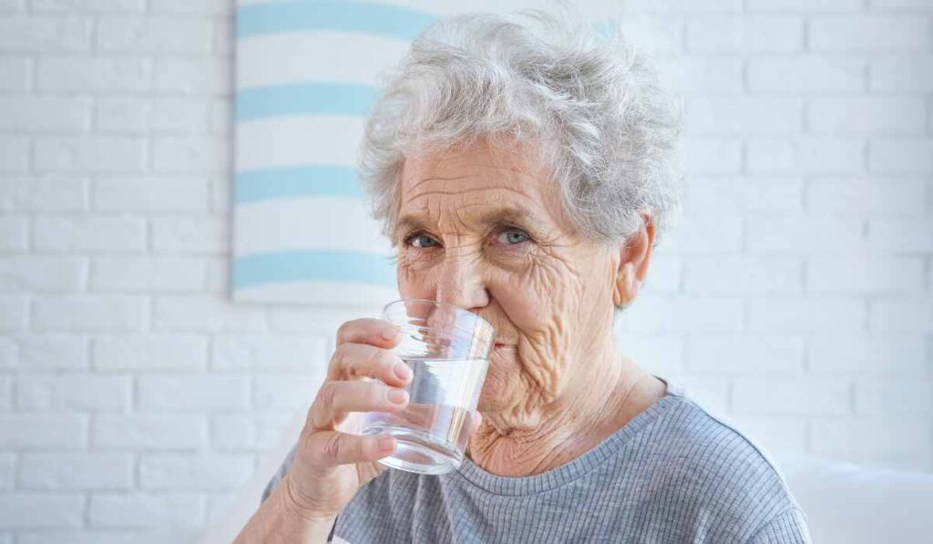 Uma senhora tomando um copo de água, como parte da dieta mediterrânea.