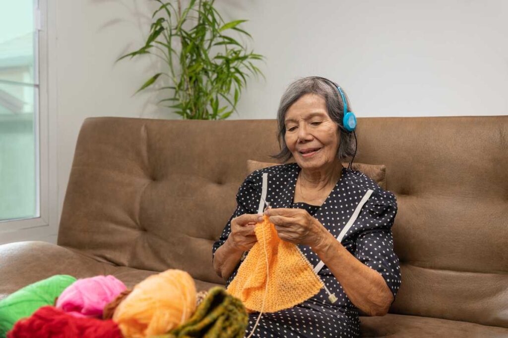 Senhora oriental fazendo tricô e ouvindo música.