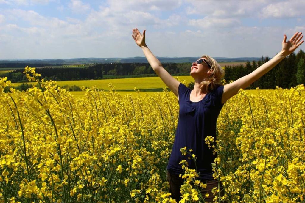 Mulher em um campo de flores amarelas. Feliz e praticando Gratidão.