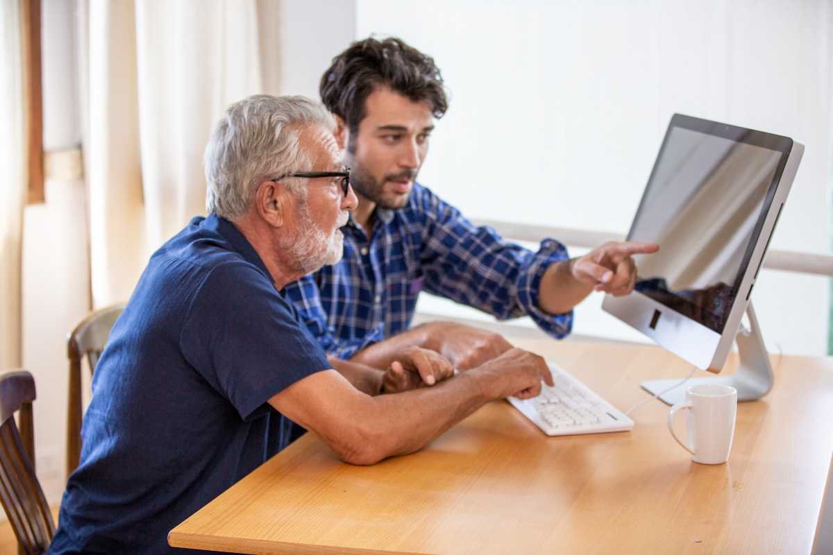 Tecnologia assistiva para idosos, um senhor e um jovem sentados à mesa, utilizando o computador