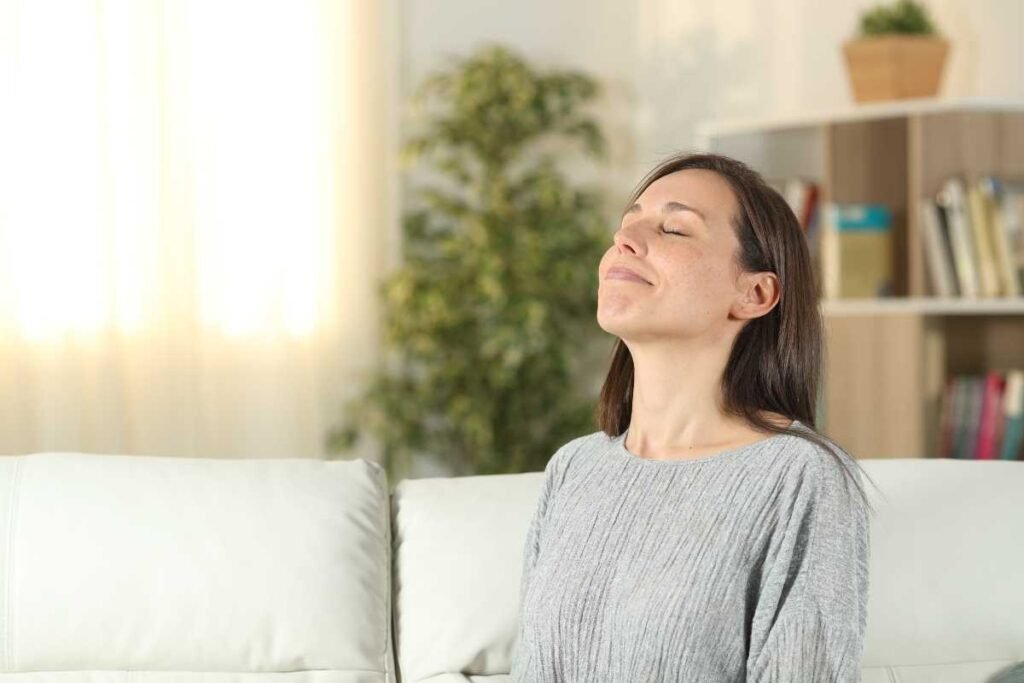 Mulher sentada em um sofá de casa,  respirando fundo e sentindo um cheiro bom.