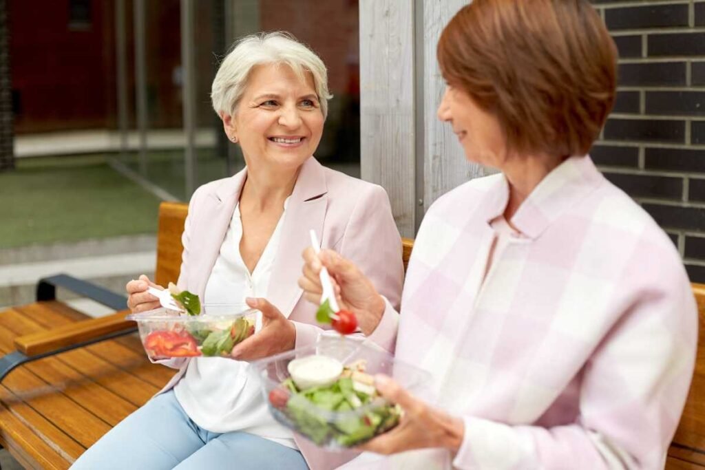 Duas senhoras sentadas num banco e se alimentando saudável para melhorar a memória